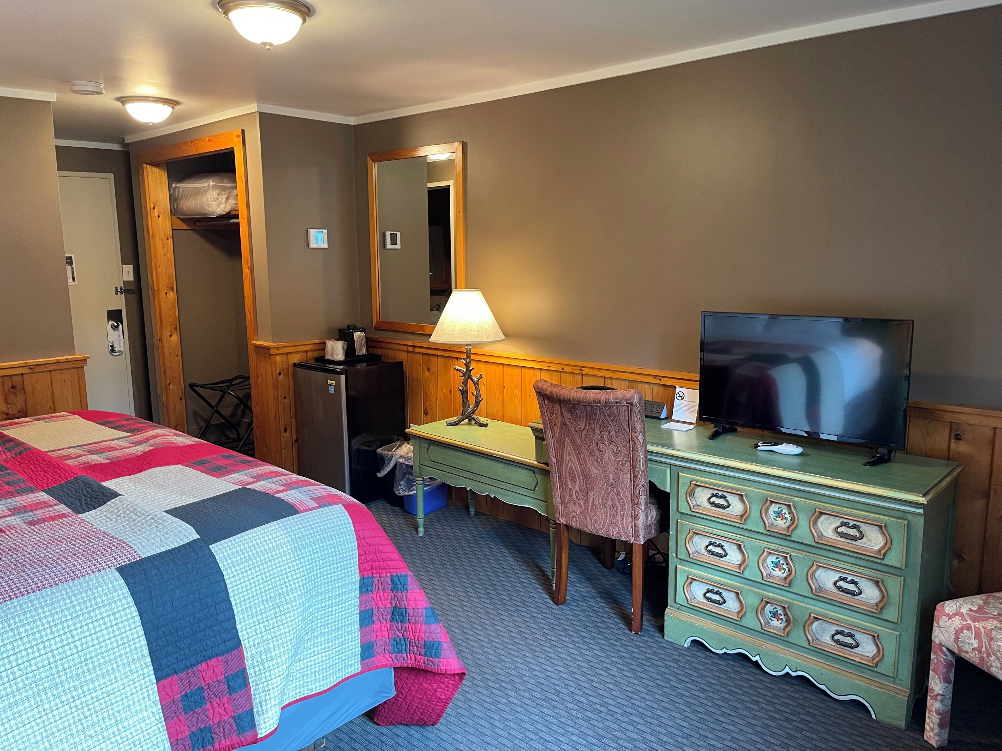 Una habitación de hotel con cama, escritorio con televisor, cómoda y espejo.