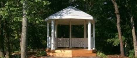 Ein Kiosk mit einer Holzdielen-Terrasse und einem schlichten Dach, umgeben von Bäumen.