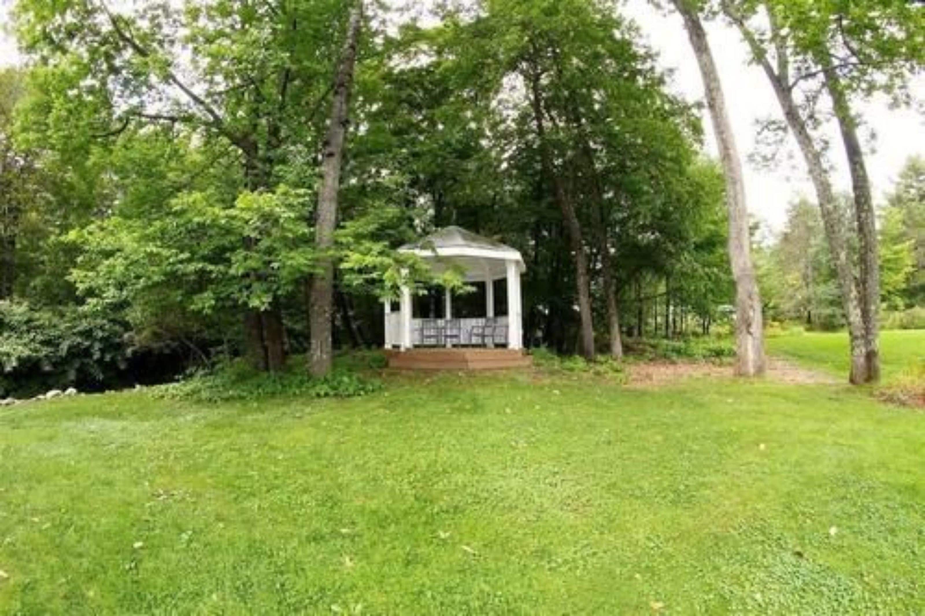A gazebo in a lush green park with trees surrounding it.