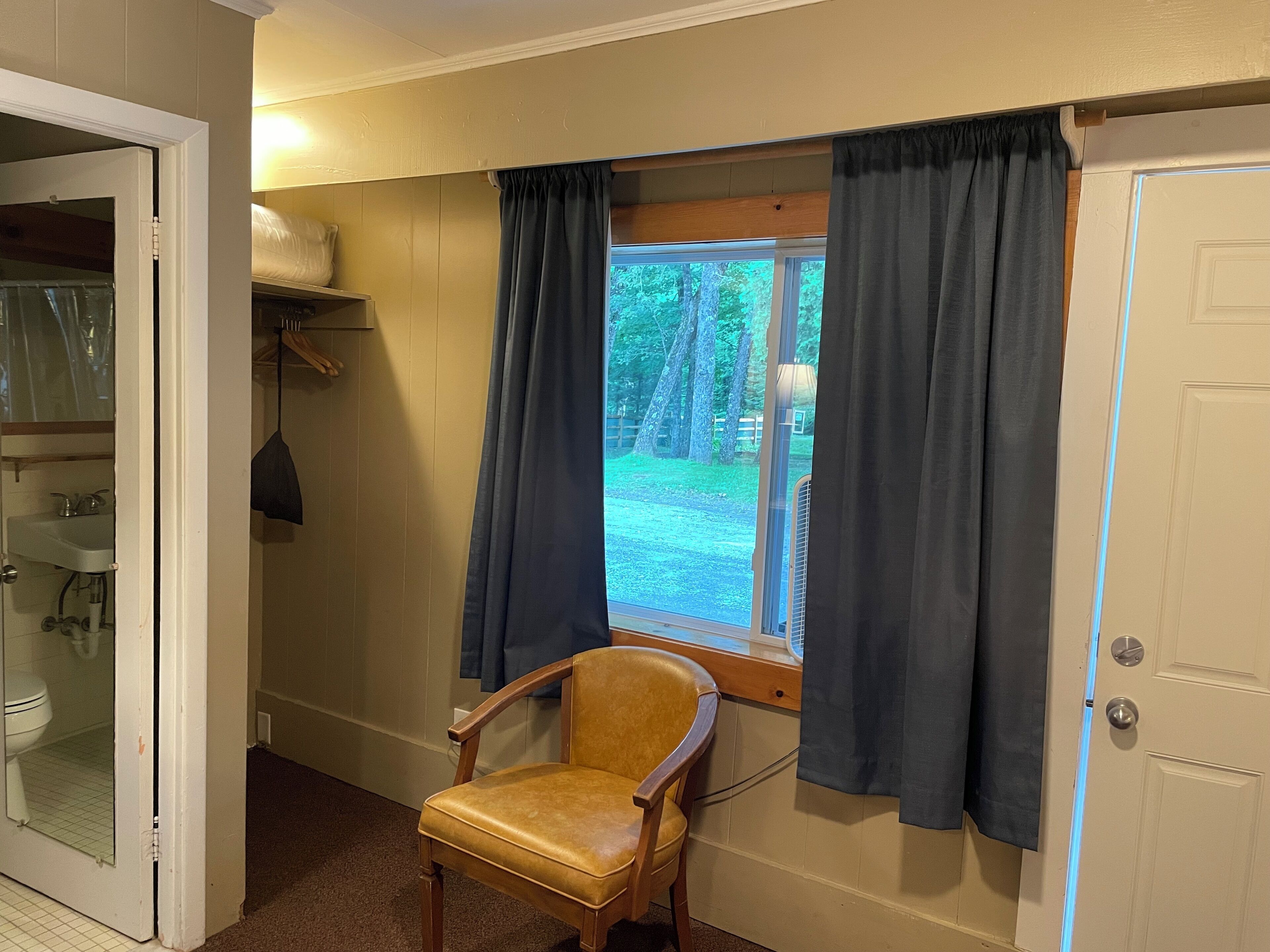 Una habitación con ventana, una silla, una puerta y una estantería con objetos.