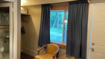 Una habitación con ventana, una silla, una puerta y una estantería con objetos.