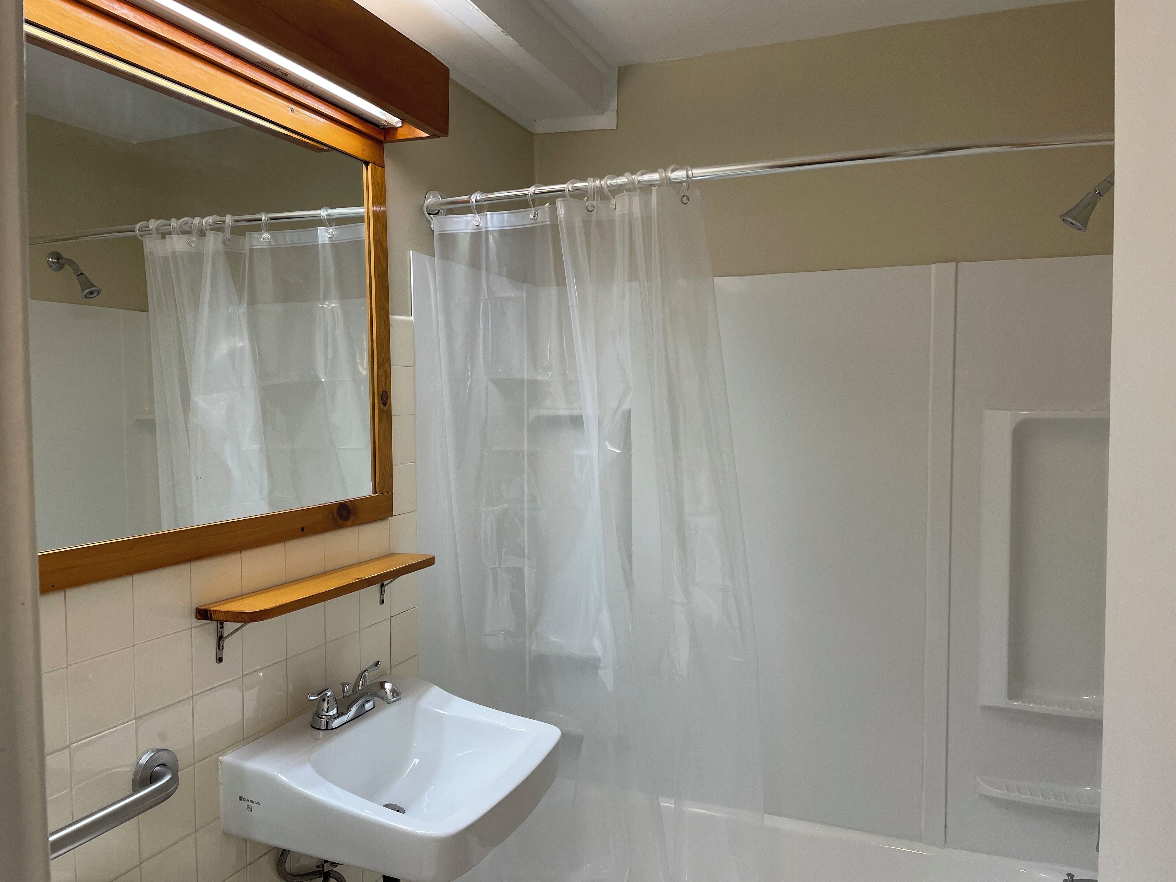 A bathroom with a white sink, a mirror with a wooden frame, a shower curtain, and a bathtub.
