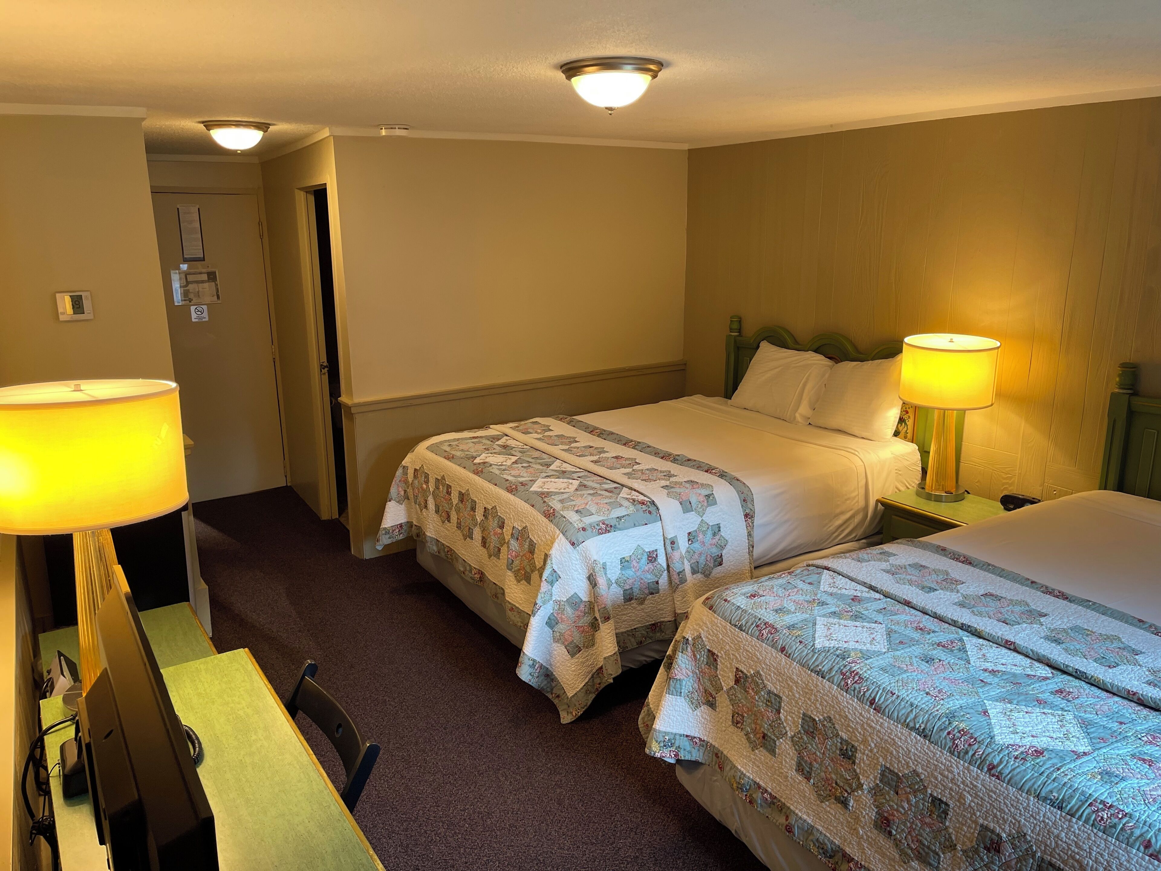 Habitación de hotel con dos camas, un escritorio y lámparas.