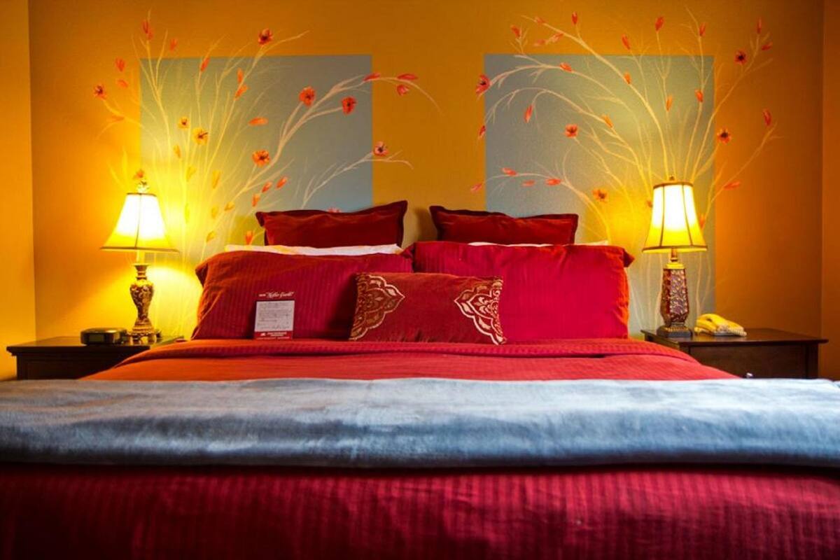 A hotel room with a large bed, red bedding, two bedside lamps, and floral wall art.