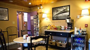 A small dining area with a table and chairs, a refrigerator stocked with beverages, and a wall-mounted coffee machine. - Anchorage Downtown Hotel (Anchorage)