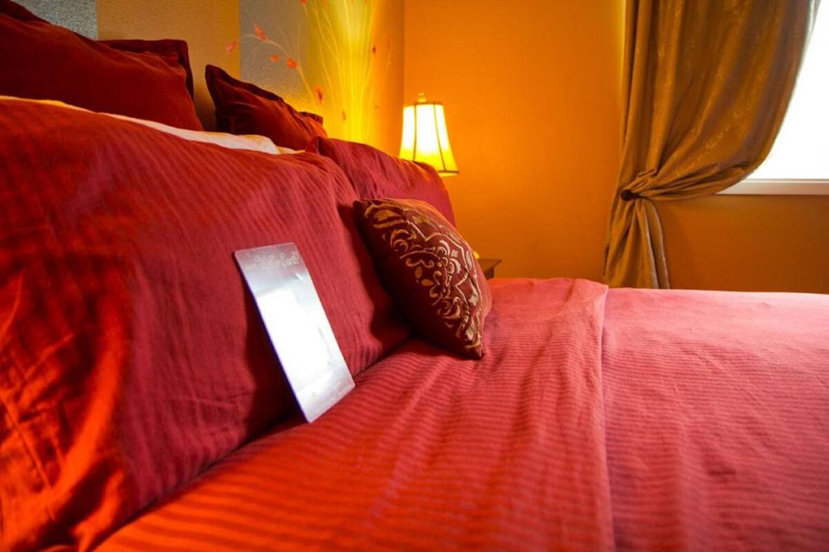 A bed with red bedding and a decorative pillow, a bedside lamp, and a window with curtains.