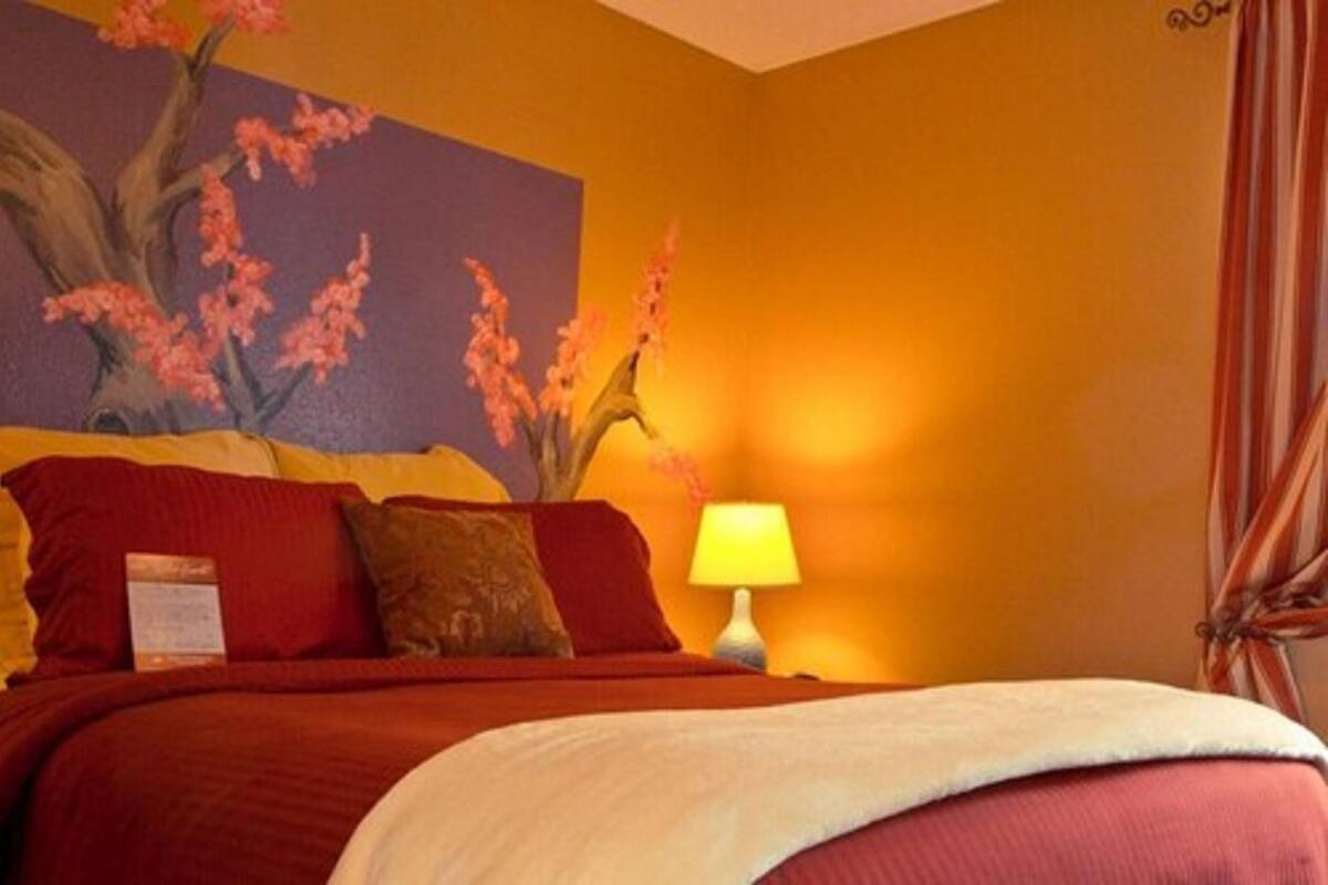 A hotel room with a bed, a nightstand with a lamp, and a painting of a tree on the wall.