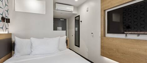 A modern hotel room with a large bed, a mounted TV, and an air conditioning unit.