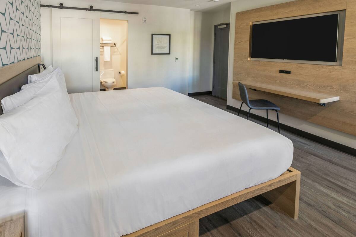 A modern hotel room with a large bed, a mounted TV, and a small seating area.