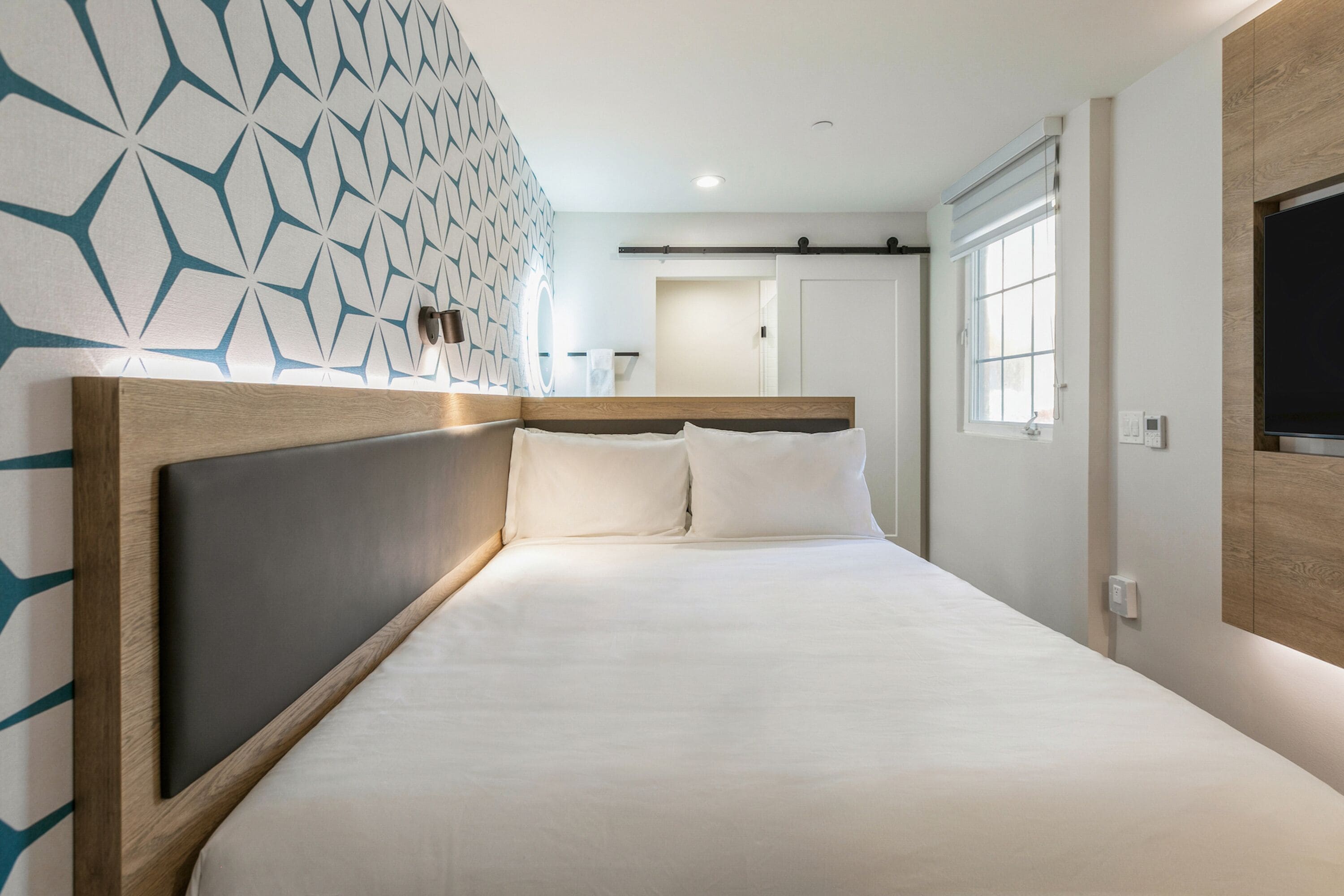 A modern hotel room with a large bed, a wooden headboard, and a geometric-patterned wall.