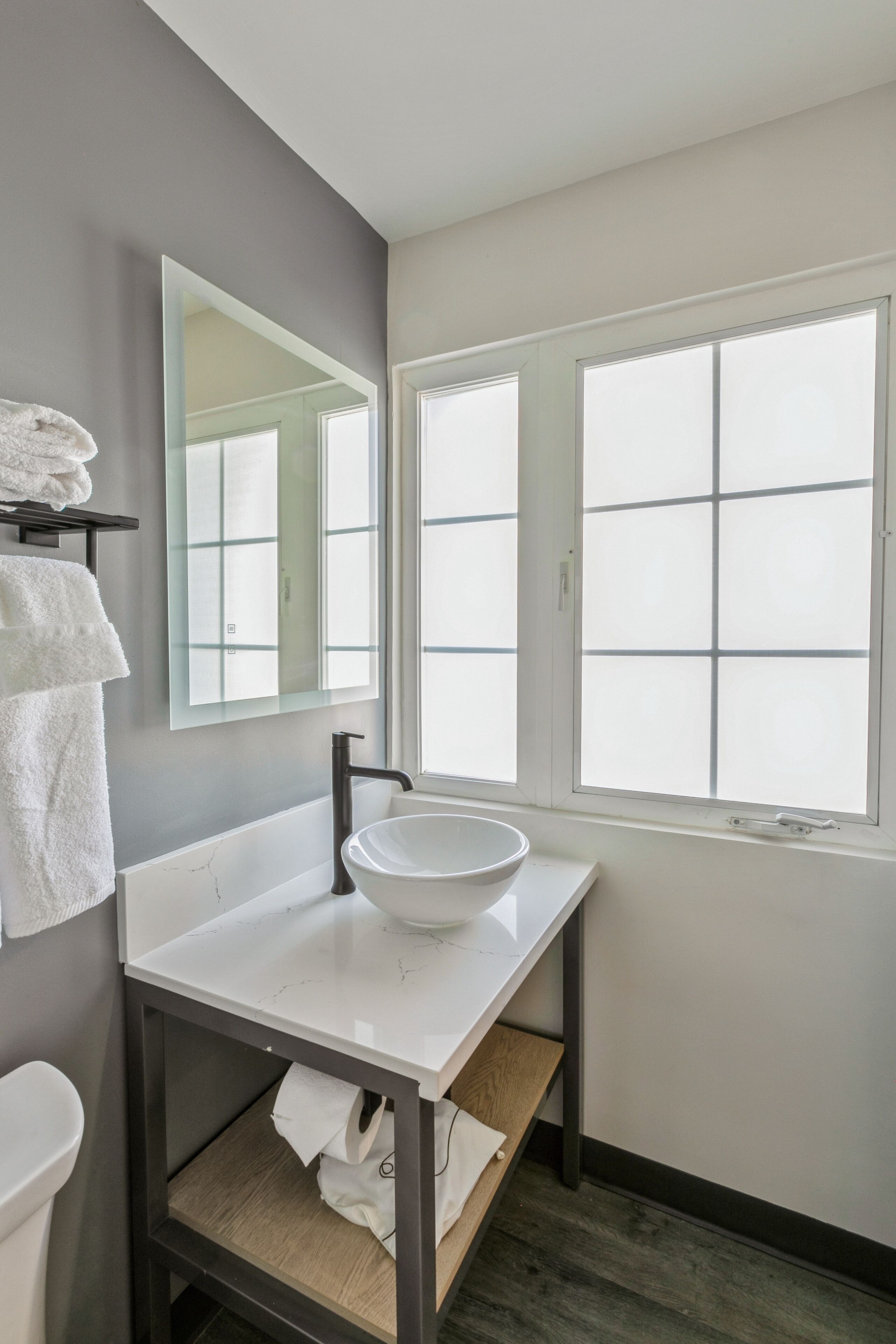 A bathroom with a white sink, a mirror, a towel rack, and a window.