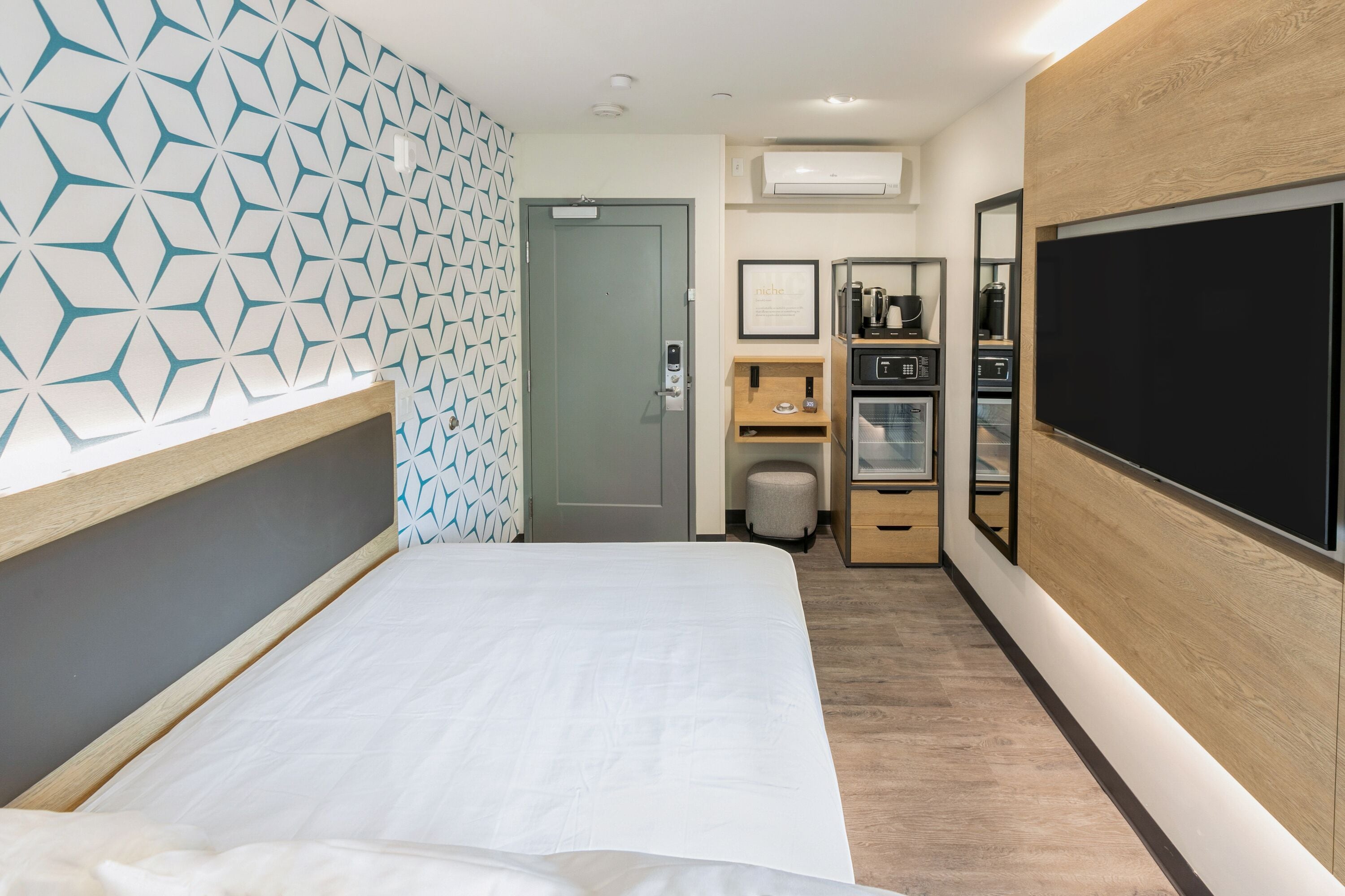 A hotel room with a bed, a minibar, a coffee machine, and a television.