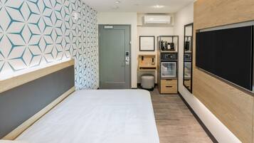 A hotel room with a bed, a minibar, a coffee machine, and a television.
