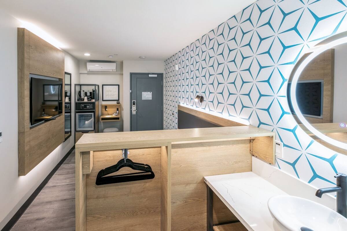 A modern bathroom with a wooden vanity, a sink, and a mirror. There is a towel rack and a door with a sign.