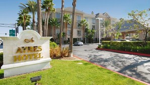 A hotel sign with a palm tree-lined driveway and a multi-story building in the background. - Ayres Hotel Anaheim (Anaheim)