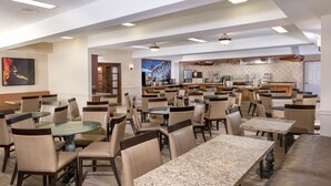 A spacious dining area with multiple tables and chairs, a kitchen in the background, and a large painting on the wall. - Ayres Hotel Anaheim (Anaheim)