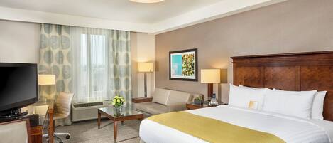 A hotel room with a large bed, a flat-screen TV, a desk with a lamp, a chair, and a window with curtains.