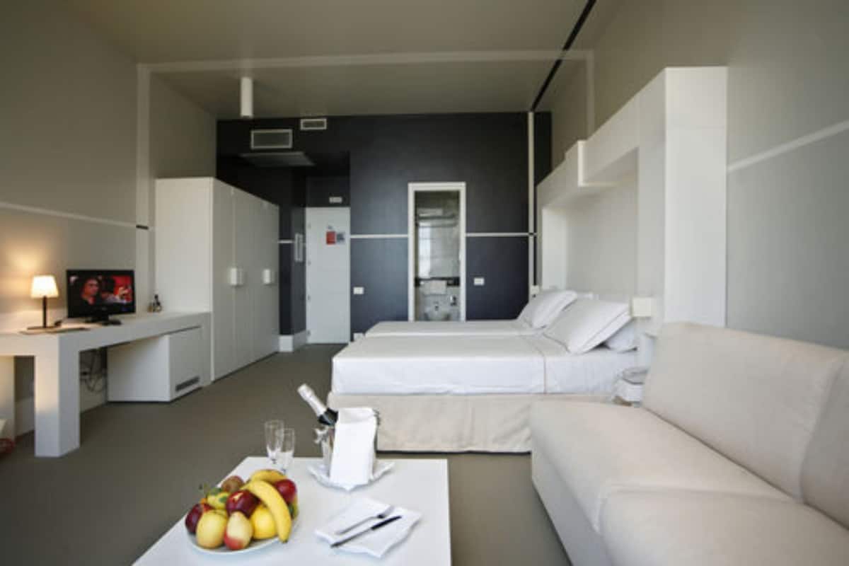 Een moderne hotelkamer met een bed, een slaapbank, een eettafel met fruit en een televisie.