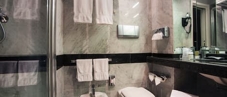 Un baño moderno con cabina de ducha de vidrio, un bidé, un inodoro y un espejo con un teléfono.