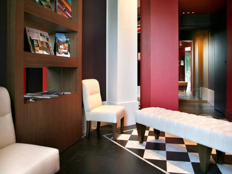 A hotel room with a checkered floor, a white sofa, a wooden bookshelf, and a bed with a white bedspread.