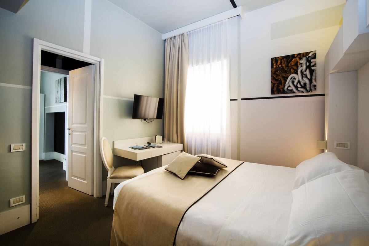 Een hotelkamer met een bed, een bureau, een stoel, een televisie en een schilderij aan de muur.