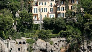 A coastal building complex with multiple balconies, surrounded by lush greenery and rocky terrain. - Hotel Piccolo Portofino (Portofino)