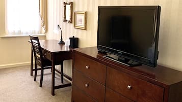 A room with a wooden desk, a television on a wooden cabinet, and a window with curtains.