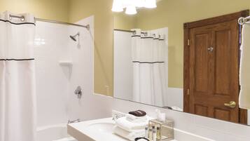 Un baño con lavamanos blanco, un espejo, ducha y puerta de madera.