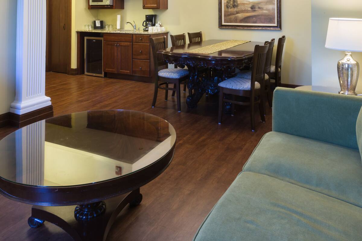 A dining area with a glass-top table, wooden chairs, a chandelier, and a painting on the wall.