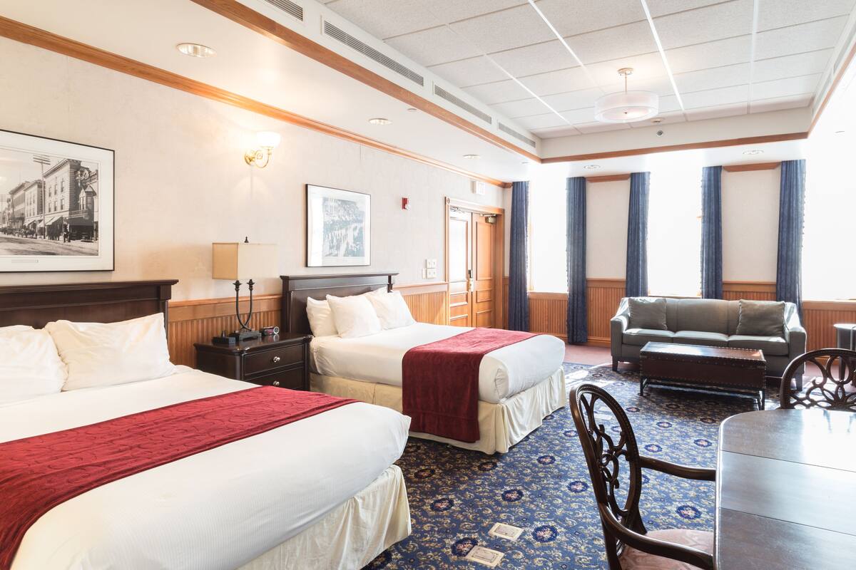 A hotel room with two beds, a sofa, a dining table, and a chandelier.