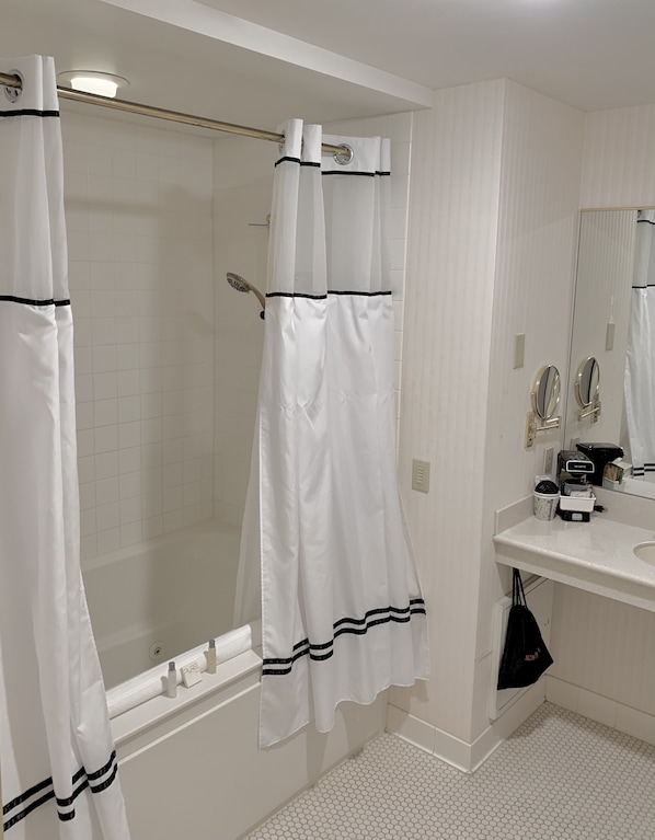 A bathroom with a bathtub, a shower curtain, a sink with a mirror, and a towel rack.