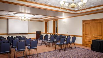 Un salón de conferencias con filas de sillas azules, una pantalla de proyector y una puerta de madera.