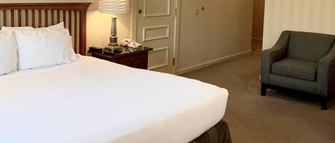 A hotel room with a large bed, a bedside lamp, a telephone, a chair, and a door.