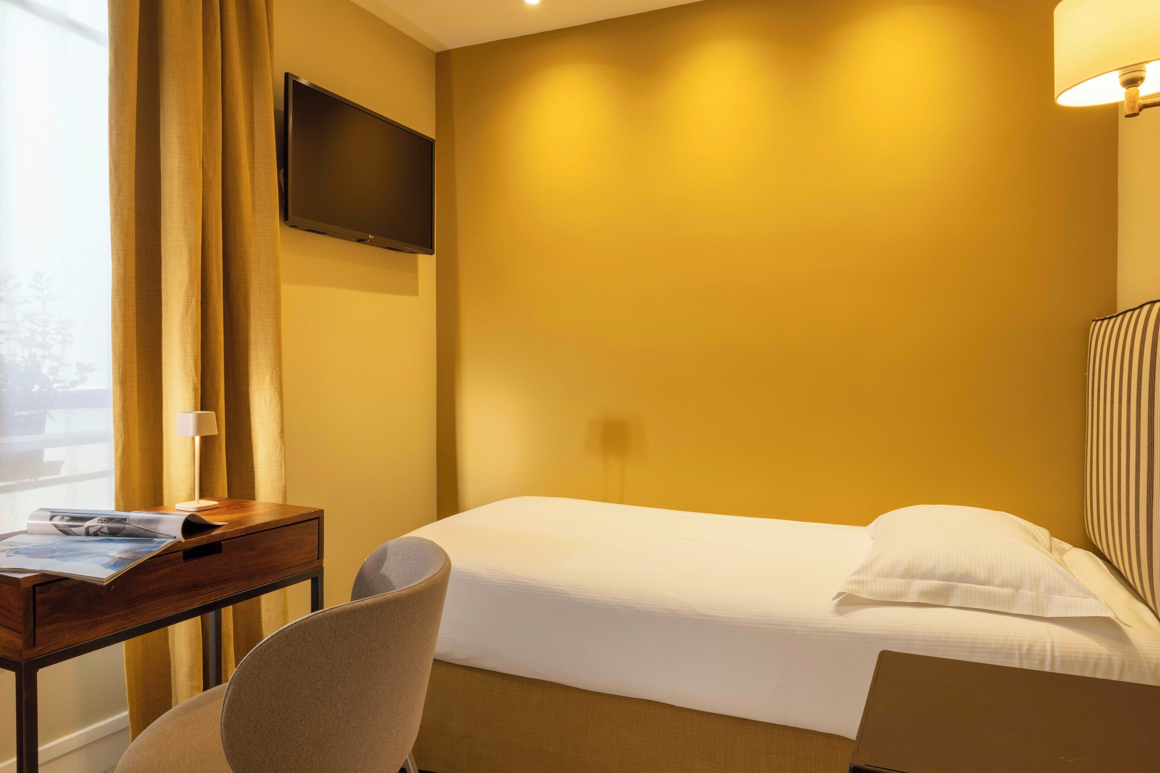 Una habitación de hotel con una cama, un escritorio con lámpara, una silla y un televisor en la pared.