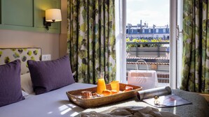 A hotel room with a bed, a breakfast tray, a window with curtains, and a city view. - Hôtel Clément (Paris)
