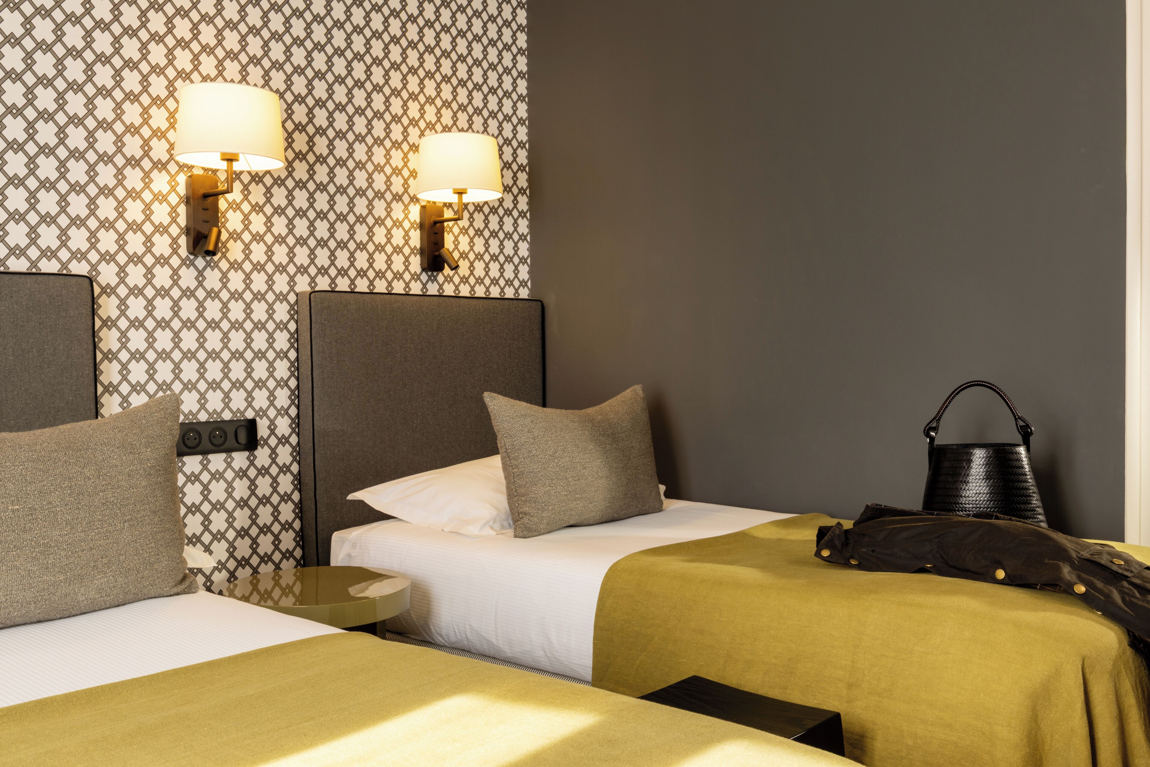 A hotel room with two beds, a nightstand, a lamp, and a handbag.