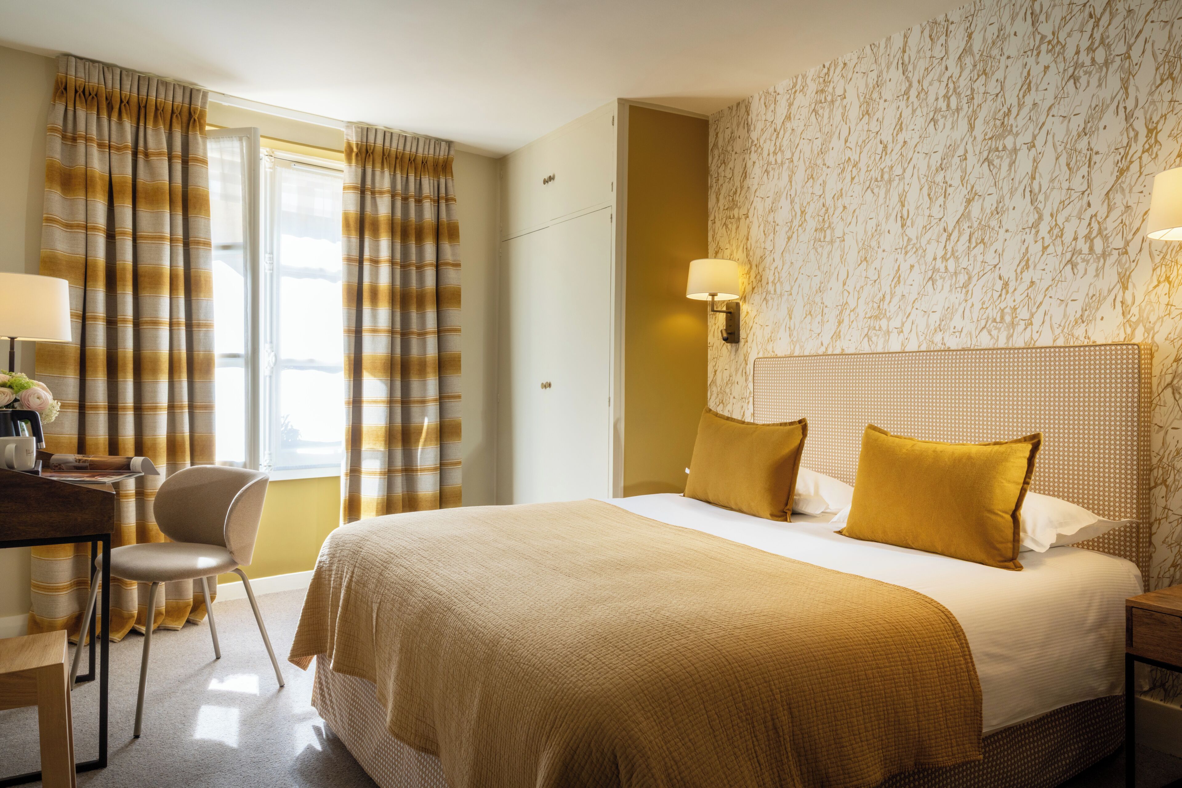 A hotel room with a bed, a desk, a chair, and a window with curtains.