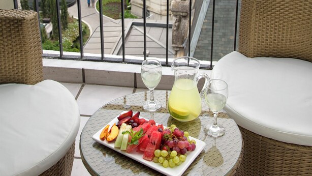 A balcony with wicker furniture, a glass table, and a plate of fruit and a pitcher of lemonade. - Hotel Sheltown (Buenos Aires)