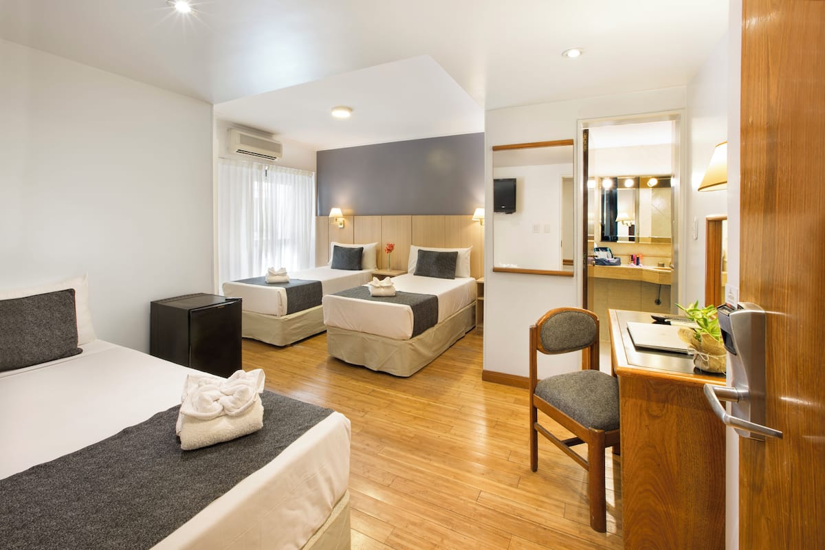 Una habitación de hotel con una cama grande, dos camas más pequeñas, un escritorio con silla, un espejo y un equipo de aire acondicionado.