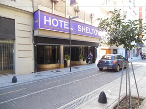 Un hotel llamado SHELTOW con una fachada moderna, grandes ventanales y una entrada visible.