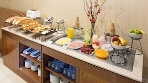 A buffet with various food items, a fruit bowl, and a vase with branches. - Hotel Sheltown (Buenos Aires)