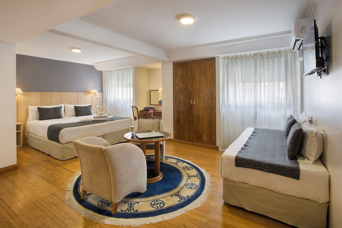 Una habitación de hotel con cama, sofá, sillón, una mesita y un tapete redondo.