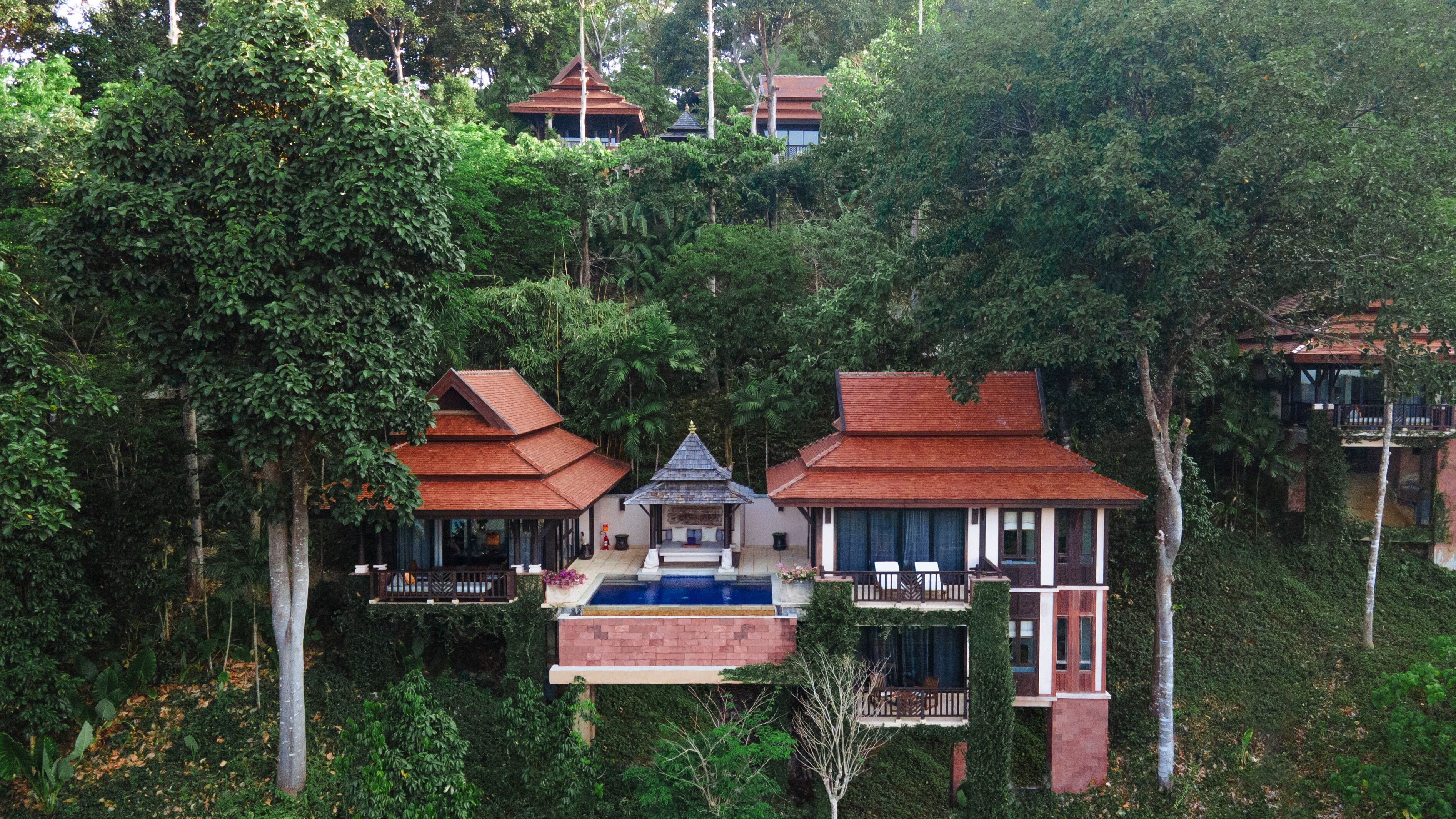 Un complexe hôtelier composé de plusieurs bâtiments entourés d’une forêt dense, avec une piscine centrale et une architecture de style traditionnel.