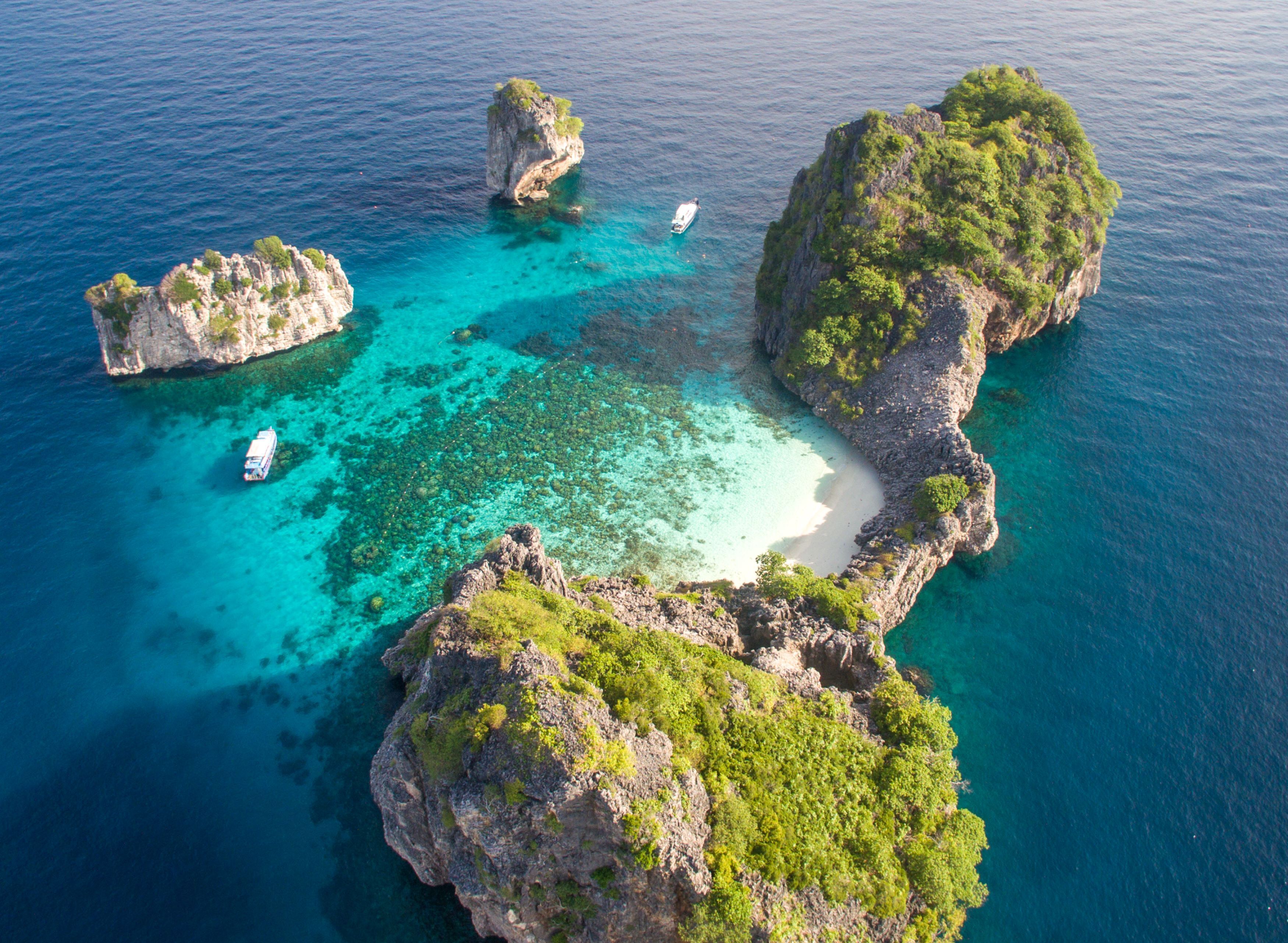 An aerial view of a coastal area with rocky formations, clear turquoise waters, and a sandy beach.