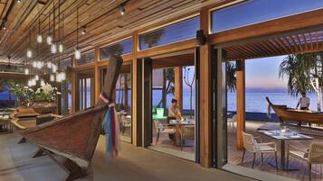 A modern restaurant with large windows overlooking the sea, wooden interior, and a dining area with tables and chairs.