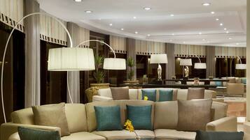 A modern hotel lobby with a large seating area, multiple lamps, and decorative plants.