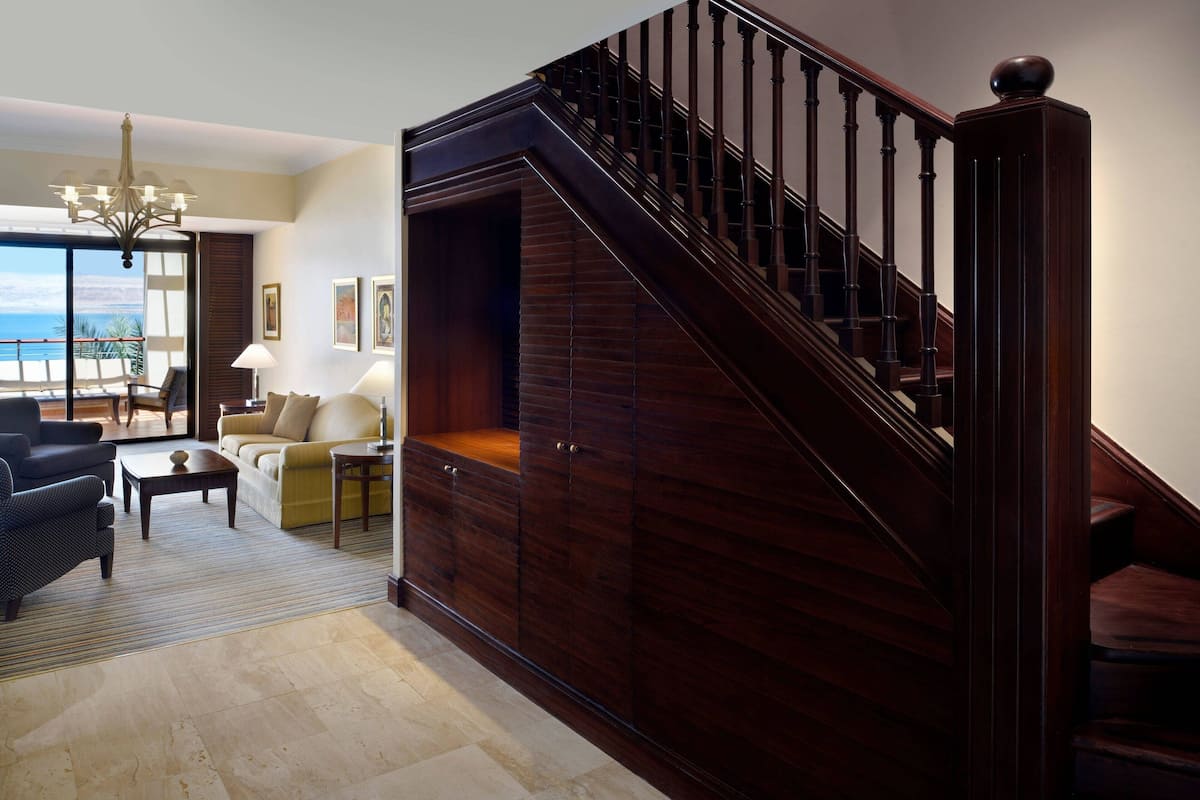 A spacious living room with a staircase, a chandelier, and a view of the ocean.