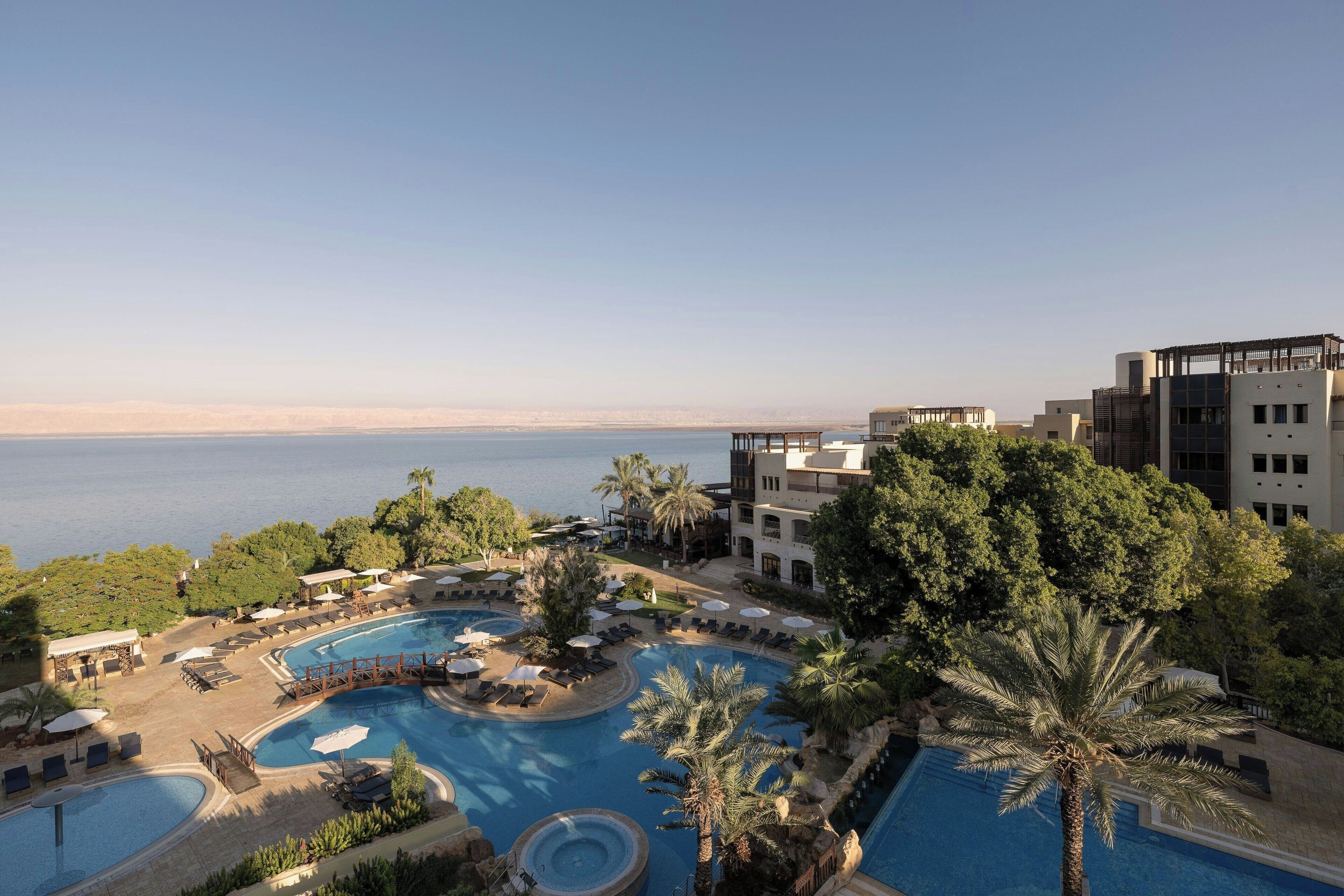 Un resort con una amplia zona de piscina, palmeras y vistas al mar.