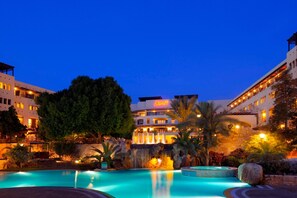 Un hotel con piscina, cascada y fachada bien iluminada.