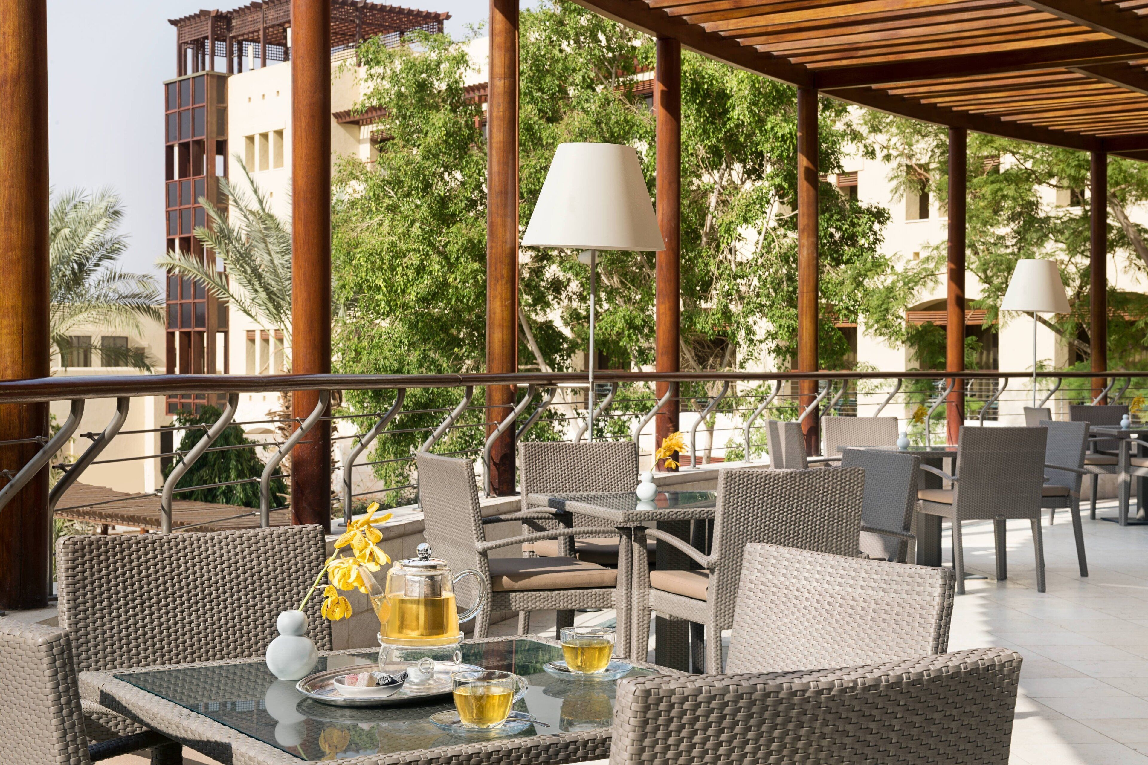 An outdoor seating area with wicker furniture, a glass table, and a view of buildings and trees.